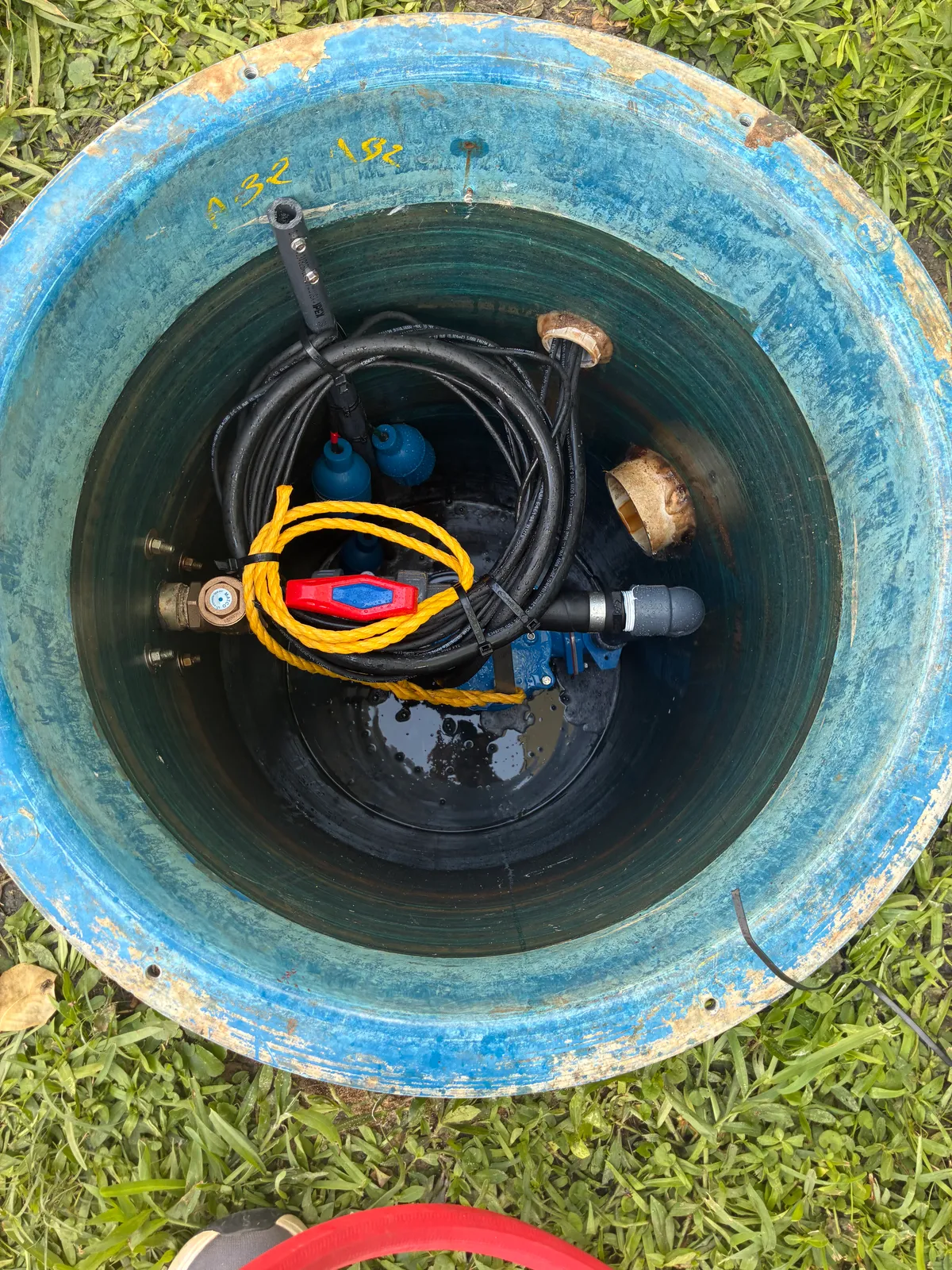 A grinder pump station opened up in its basin, showing the pump, float switch, and discharge piping