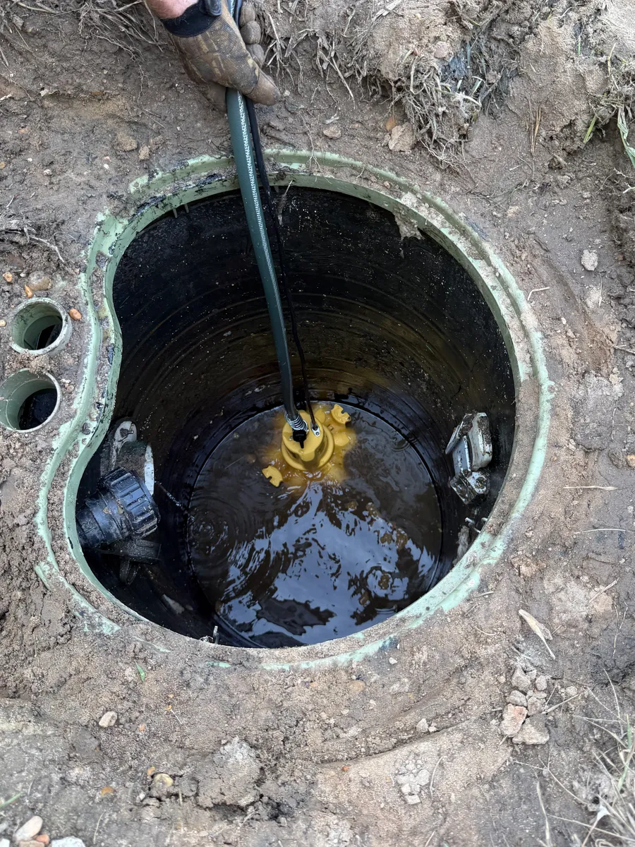 Looking straight down into a grinder pump basin with the replacement pump set on the bottom, its yellow discharge connection above the water line