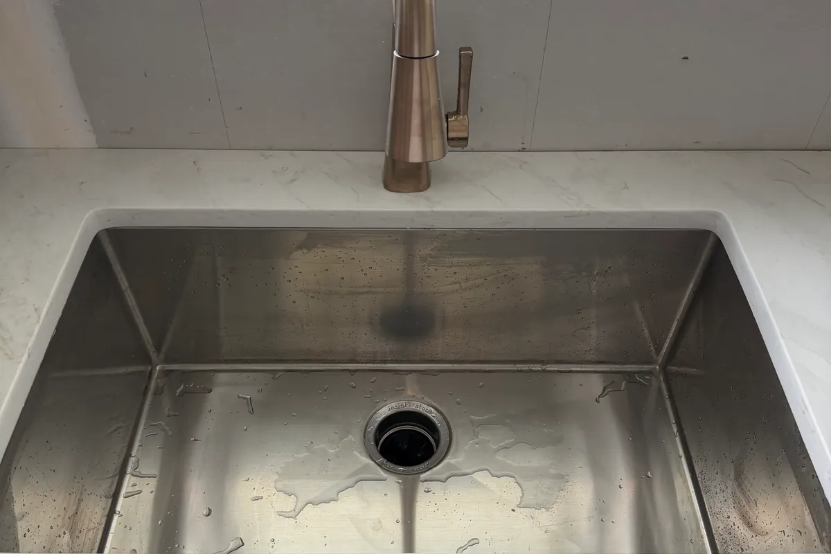A set stainless undermount kitchen sink and brushed-nickel pull-down faucet in a quartz countertop, basin still wet from the first test run